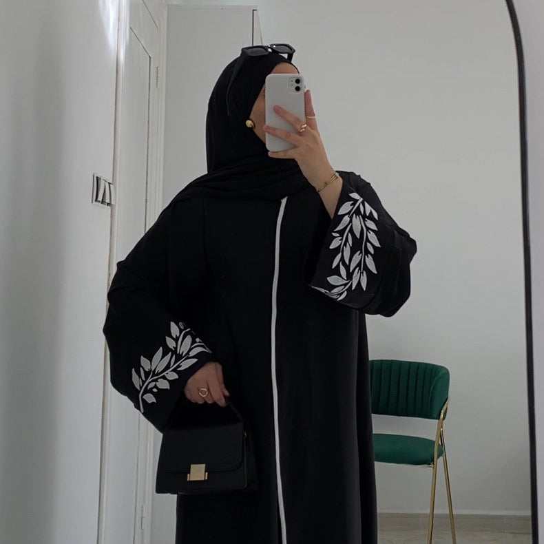 Person wearing a black outfit with white patterns in a room with a mirror and chair.